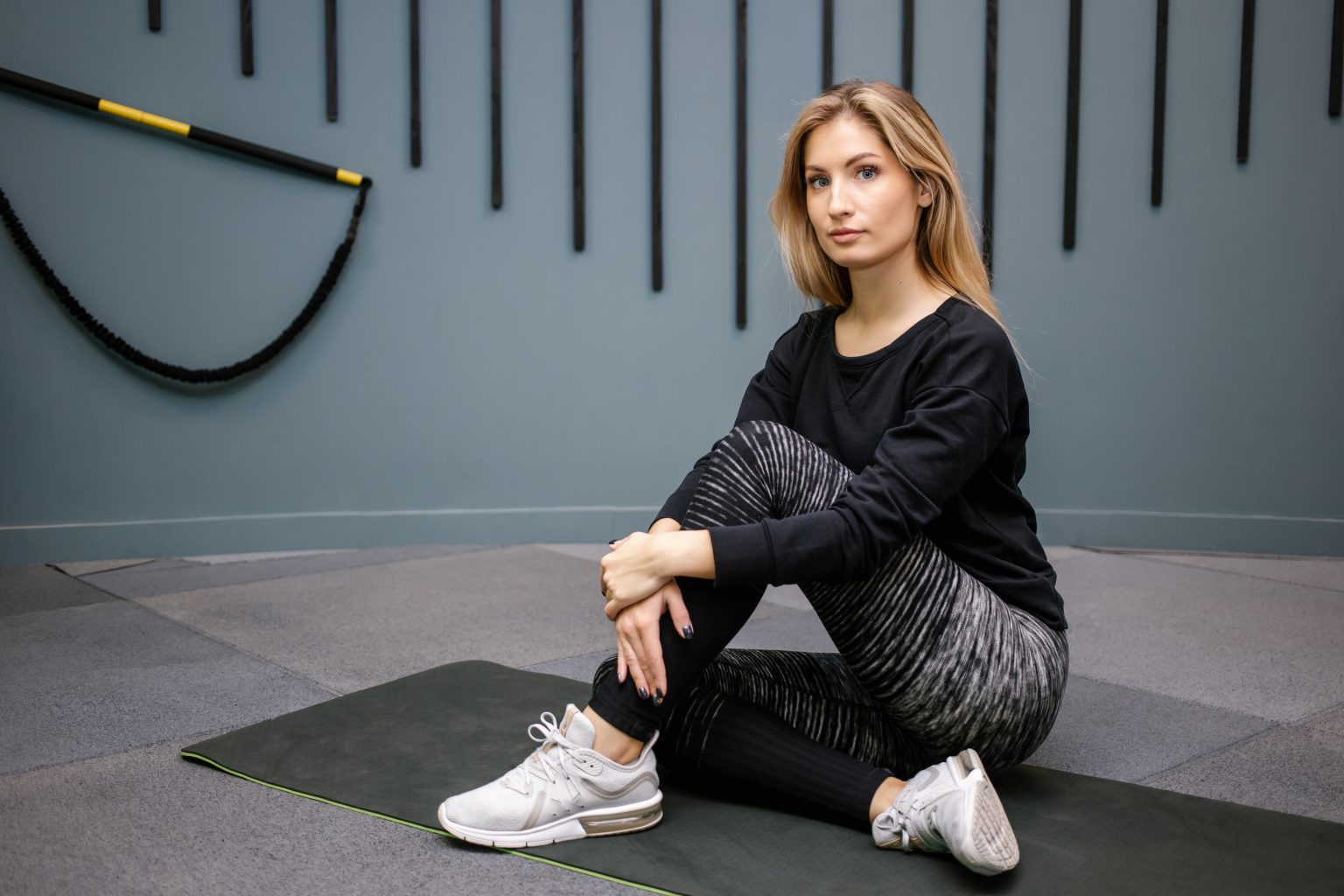 Attractive happy woman sitting on the floor after exercise on gym background. Concept of slim and healthy girl workout.