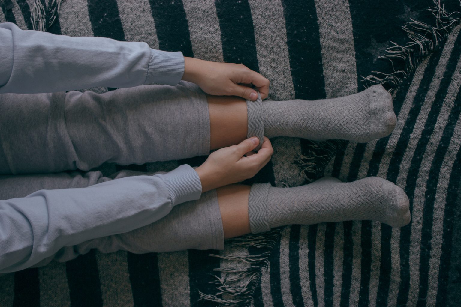 A top view of a young female putting on some socks on a cold day to spend at home. Cozy Home Concept.